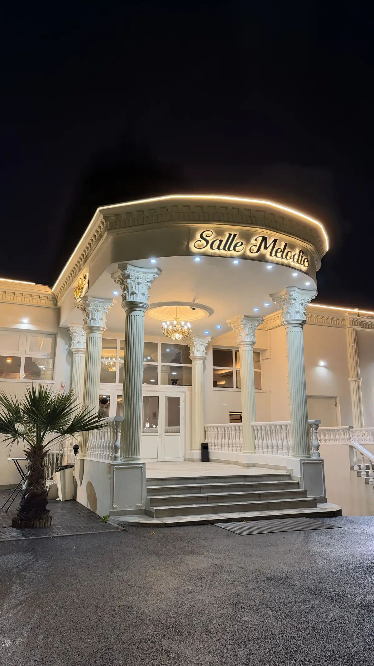 La façade de la Salle Mélodie illuminée le soir, colonnes et enseigne dorée